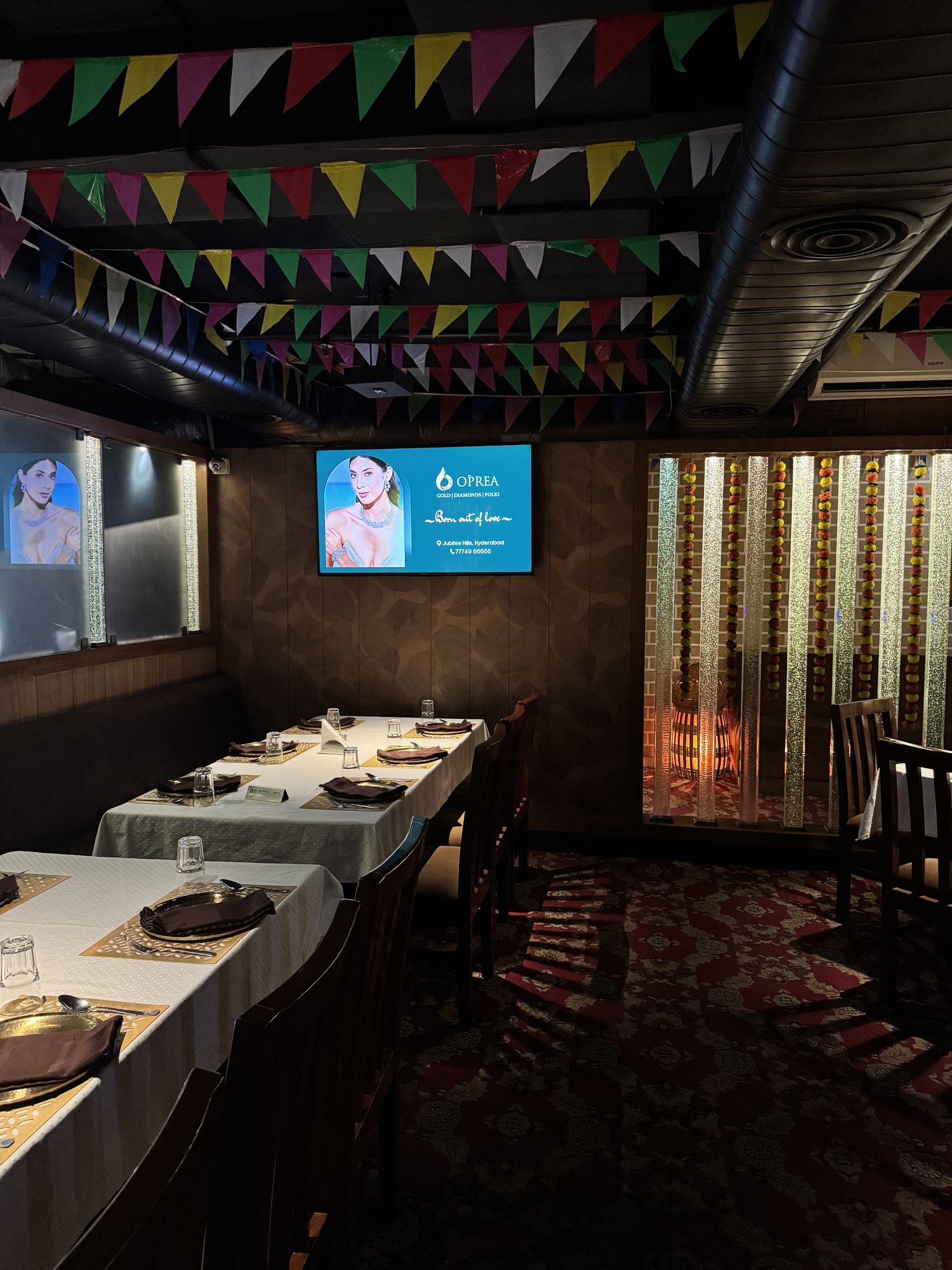 Oprea jewellery advertisement on KMEDIA screen in a festive dining room