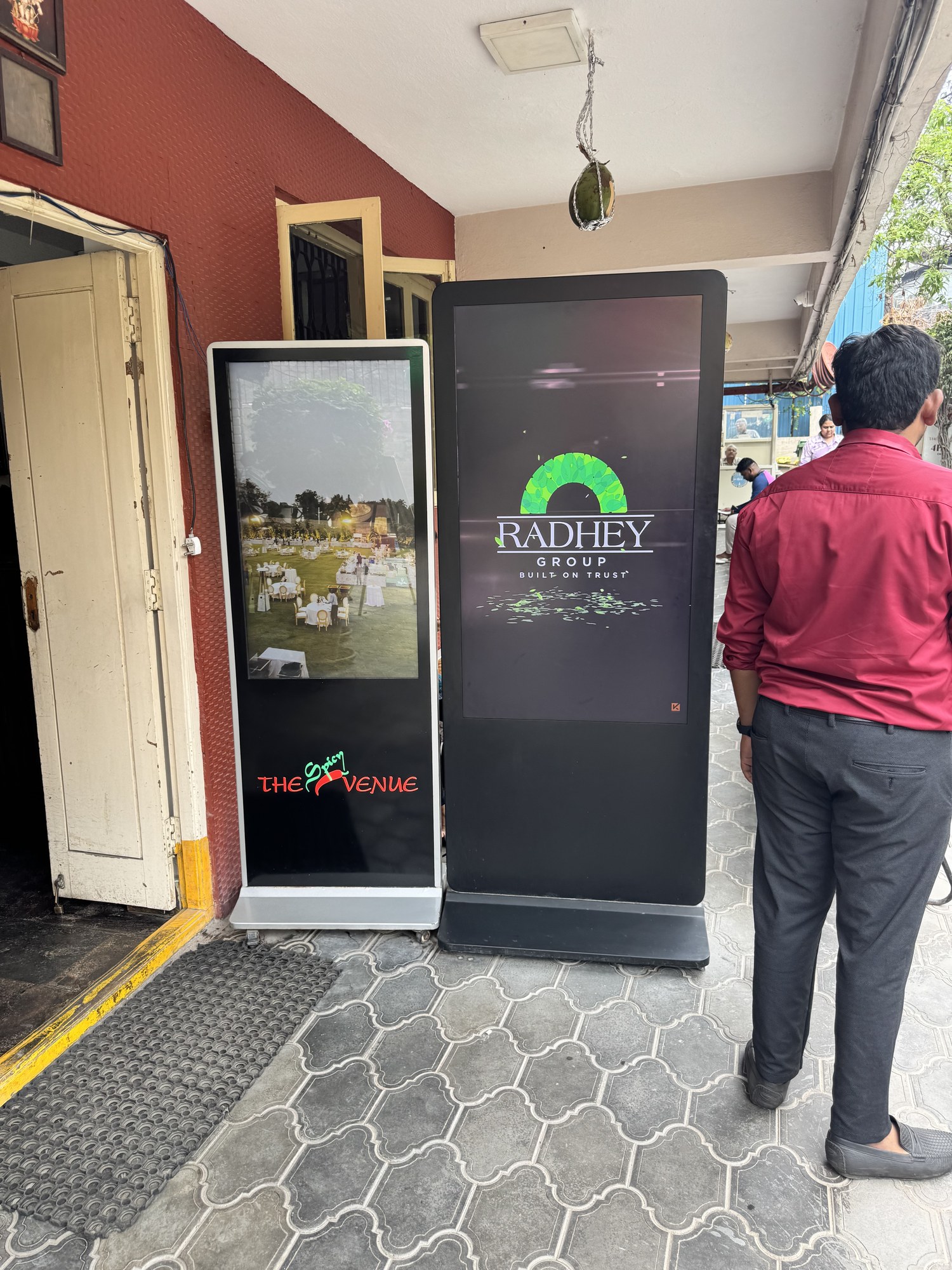 KMEDIA digital standees with Radhey Group and The Spicy Venue ads at a restaurant entrance